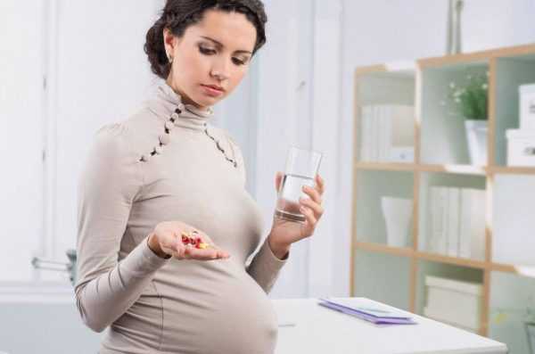 Беременная женщина с таблетками и стаканом воды