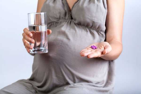 Беременная держит в руках таблетки и стакан с водой