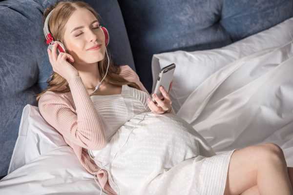 Беременная девушка в наушниках слушает музыку