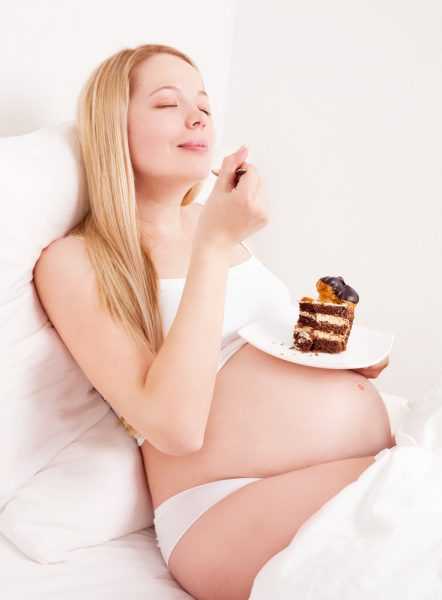 беременная подносит ложку ко рту, на тарелке кусок торта