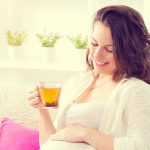 Беременная пьёт чай и поглаживает живот