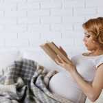Беременная полулёжа на диване читает книгу