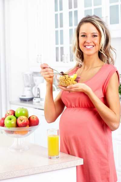 беременная с тарелкой мюсли стоит рядом с яблоками и соком
