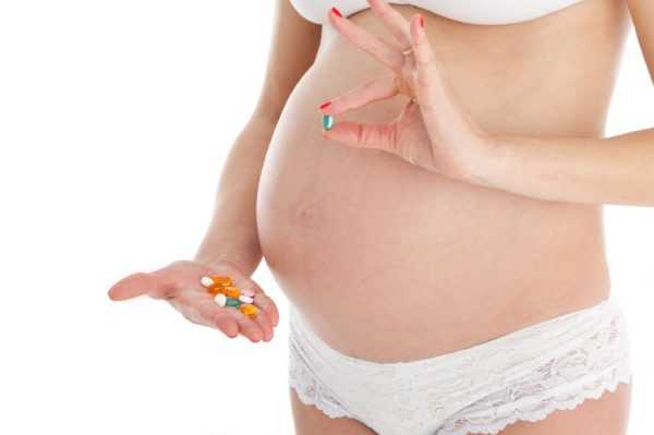 Беременная в белом белье держит разноцветные таблетки
