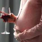Беременная женщина держит в руках бокал вина
