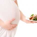 Беременная женщина держит в руках тарелку с красной рыбы