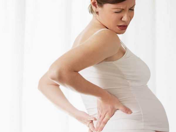 Беременная женщина держится за поясницу