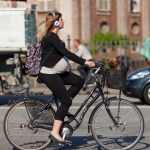 Беременная женщина едет на велосипеде с высоким рулём и вертикальной посадкой