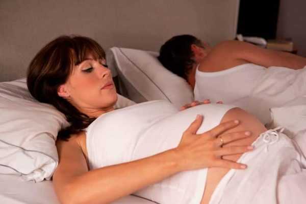 Беременная женщина лежит в постели с мужем и трогает живот