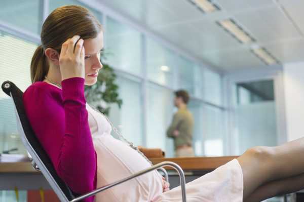 Беременная женщина сидит на стуле и держится за голову