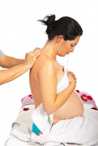 Беременная женщина сидит придерживая грудь, а на её спине лежат руки массажиста