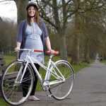 Беременная женщина стоит возле велосипеда и улыбается