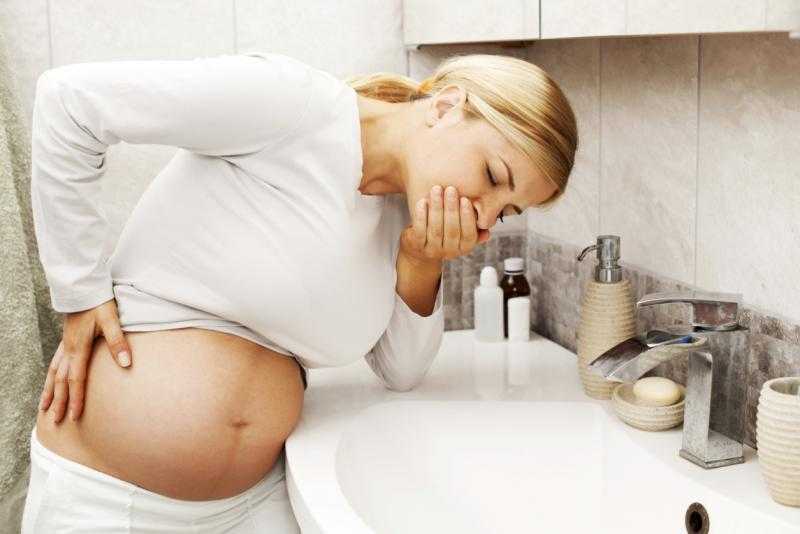 Беременная женщина зажала рот ладонью и склонилась над раковиной