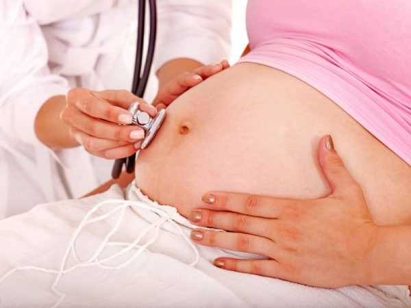 Доктор фонендоскопом слушает живот беременной