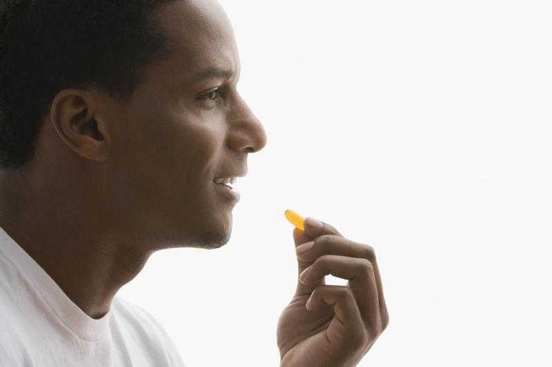 Мужчина держит пальцами таблетку возле рта