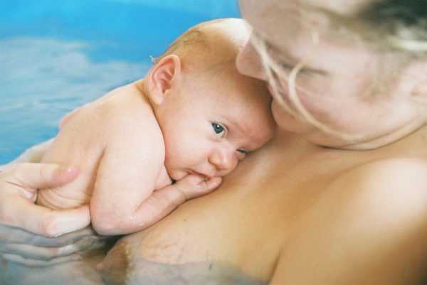 Новорожденный на руках матери, лежащей в бассейне