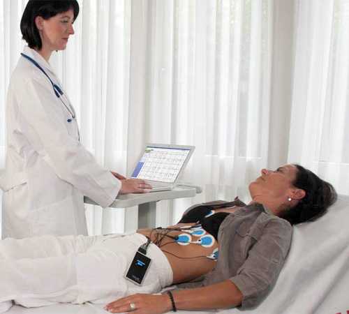 Фотография лежащей на кушетке женщины, рядом с которой стоит врач, фиксирующий результаты ЭКГ