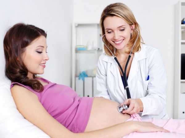 Беременная женщина лежит, а врач прослушивает её живот