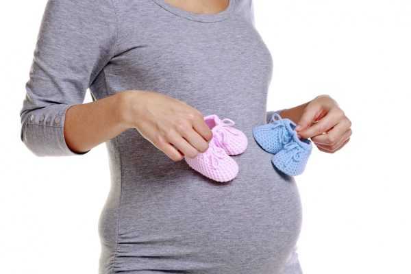 Беременная женщина держит пинетки розового и голубого цвета