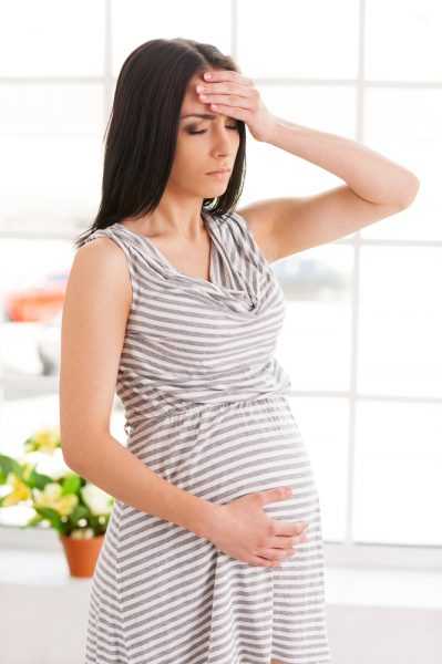Беременная женщина держится за лоб и живот