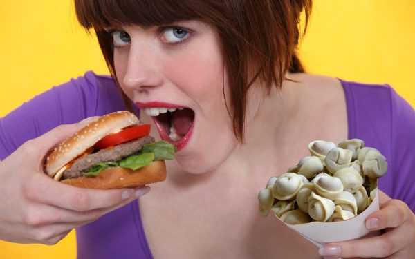 девушка подносит ко рту гамбургер