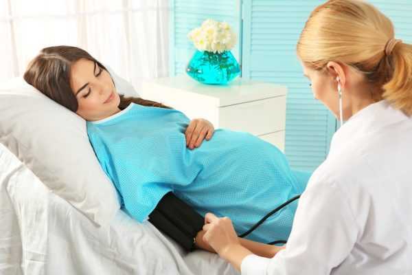беременная в халате лежит, врач измеряет давление