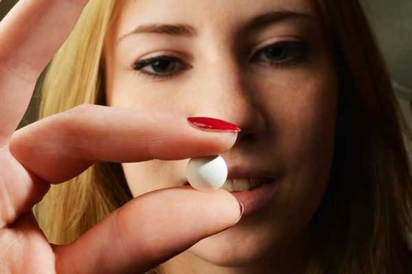 девушка держит таблетку двумя пальцами