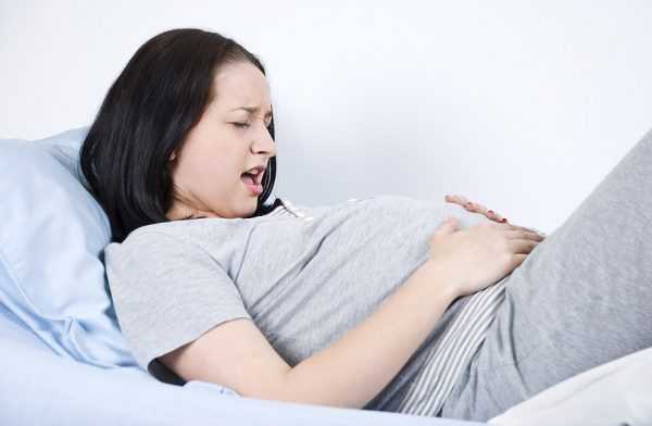 беременная держится за живот с выражением муки на лице