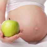 Беременная держит в руках зелёное яблоко