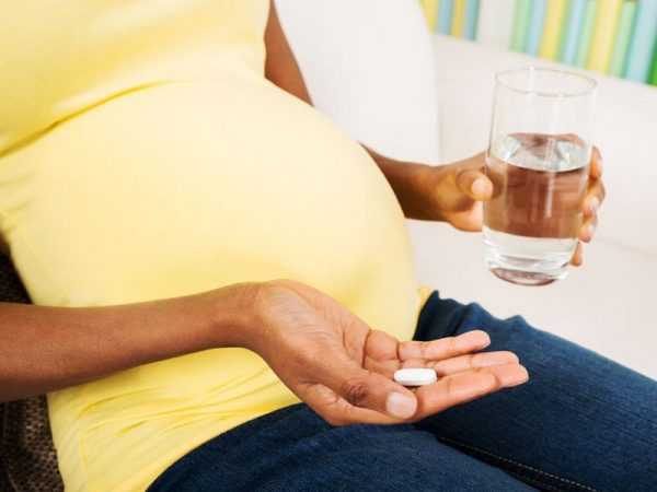 беременная держит в одной руке таблетку, в другой стакан воды