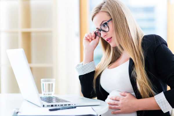 Беременная женщина смотрит в ноутбук