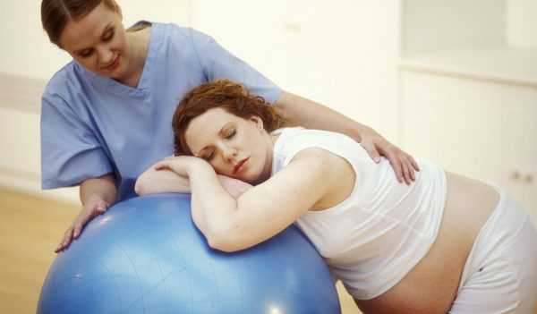 беременная женщина лежит на мяче в сопровождении медика