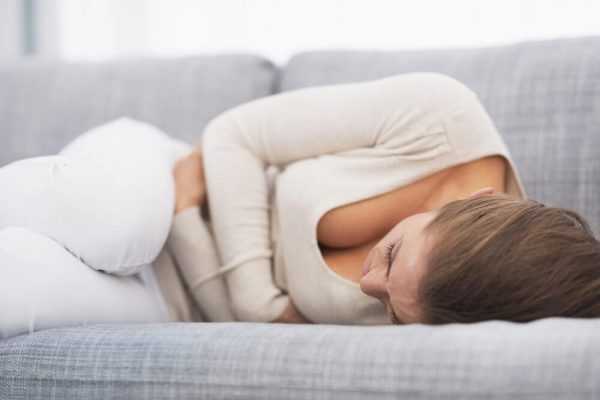 Женщина лежит на диване и обнимает живот руками