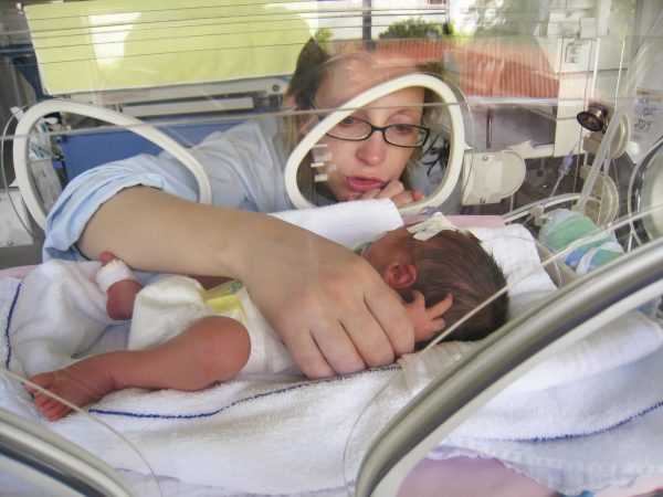 Женщина обнимает младенца в инкубаторе