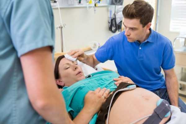 Женщина тужится во время родов в присутствии мужа и врача