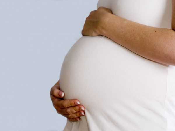 Беременная женщина в белом платье держит руками живот